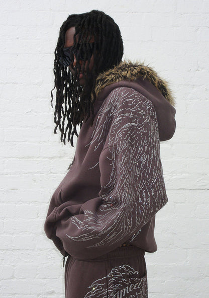 Model wearing a brown hoodie with rhinestone wing design and detachable faux fur hood, viewed from the side.