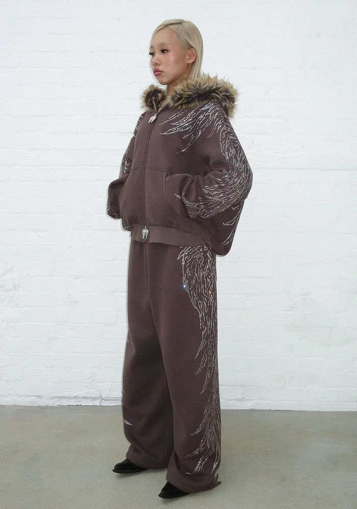 Model wearing brown sweatpants with rhinestone wing design and back pockets.