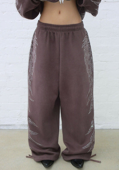 Front view of brown sweatpants featuring rhinestone wing design and adjustable ankle ties.