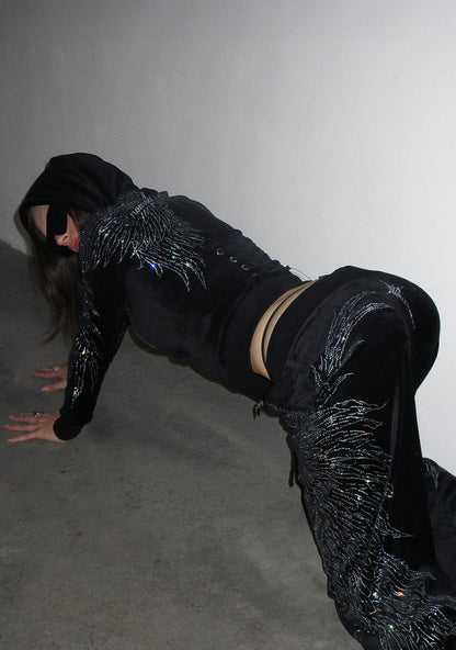 Model in black velour sweatpants with rhinestone wings, side view.