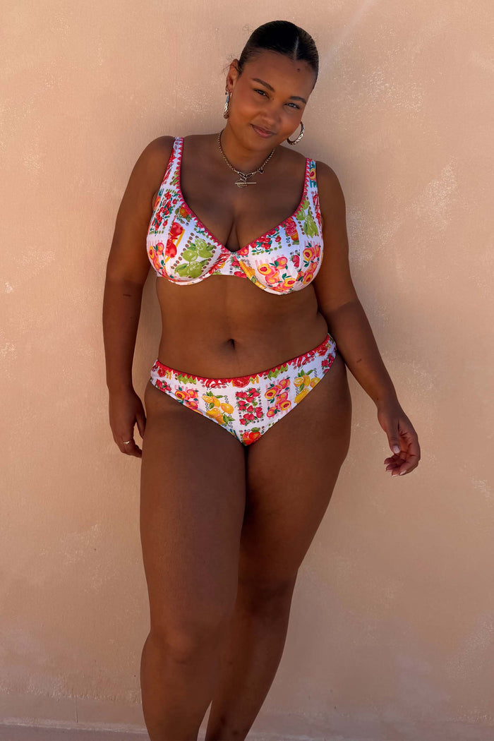 Fruit Stamps Bikini Top with a Mediterranean fruit print and pink whipstitch on a model for inclusive sizing.