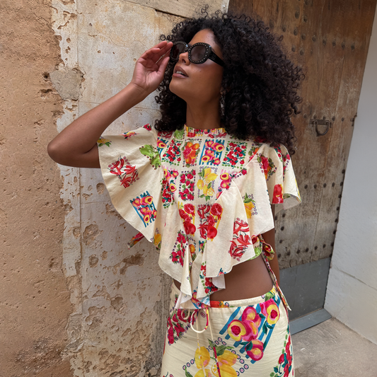 Fruit Stamps Florence Top in cream cotton-linen with a Mediterranean fruit print and ruffles, on a model in a sunny setting.