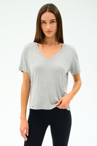 A person faces forward, wearing the SPLITS59 Georgia Jersey V-Neck in Heather Grey and black pants, standing against a plain white background.