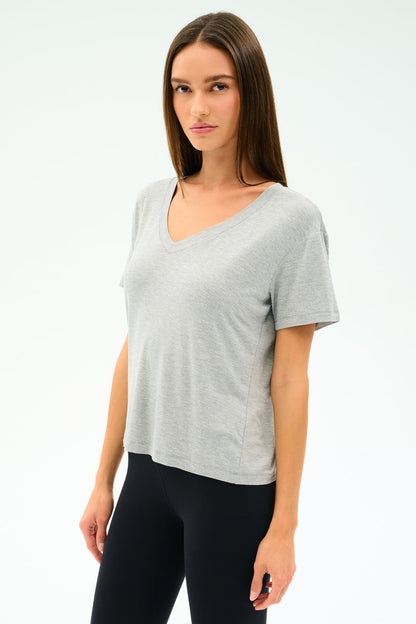 A woman faces forward against a plain white background, wearing the SPLITS59 Georgia Jersey V-Neck in Heather Grey and black spandex leggings.