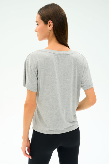 A woman with straight brown hair, wearing the SPLITS59 Georgia Jersey V-Neck in Heather Grey, stands facing away from the camera against a plain light background.