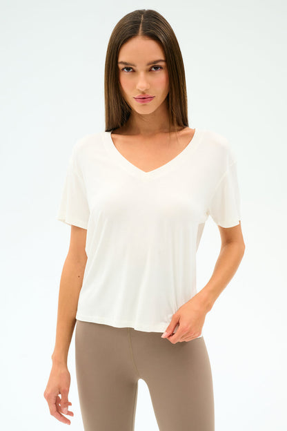 A woman wears the SPLITS59 Georgia Jersey V-Neck in white and beige leggings, standing against a plain background and looking directly at the camera.