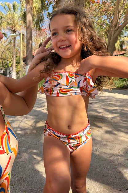 Girl's Banana Bikini featuring a multicoloured print, frill detail and red trim in a tropical setting.