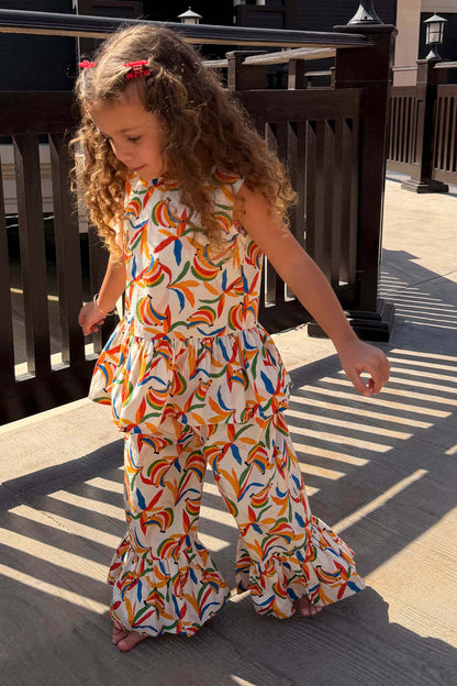 NFD Kids cream cotton banana print co-ord with a peplum top and flared frill trousers on a sunny deck.