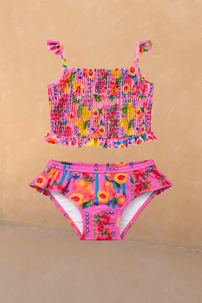 Girls pink fruit print bikini featuring a shirred bandeau top with ruffle straps and matching frilled bottoms.