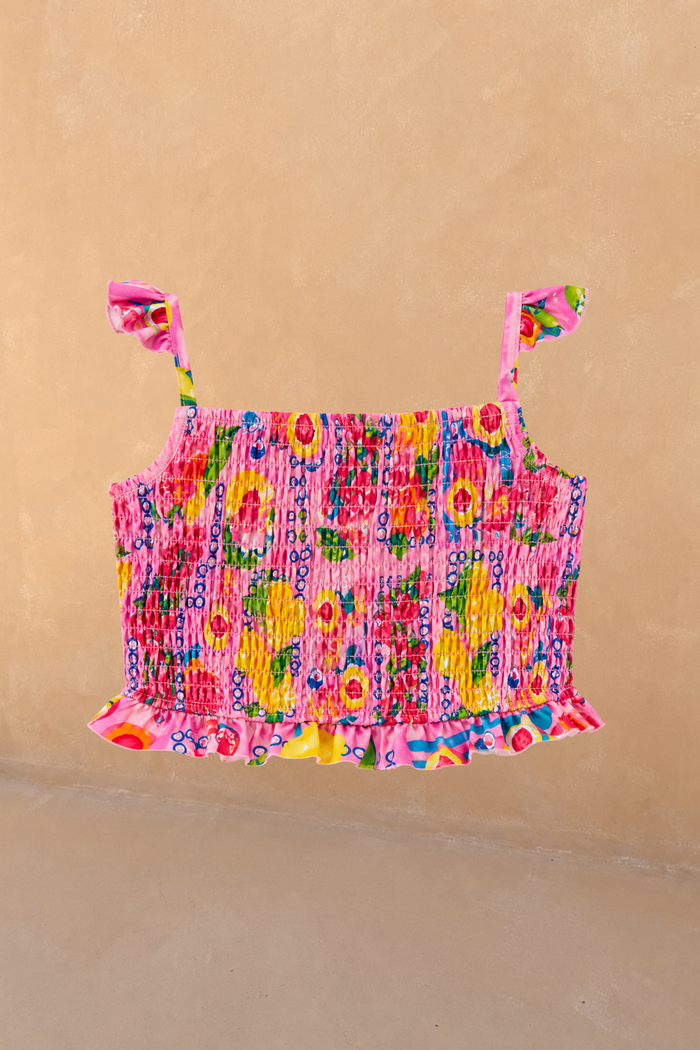 Girls Pink Fruit Crop Bikini Top featuring a shirred body and ruffle straps against a neutral wall.
