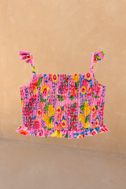 Girls Pink Fruit Crop Bikini Top featuring a shirred body and ruffle straps against a neutral wall.