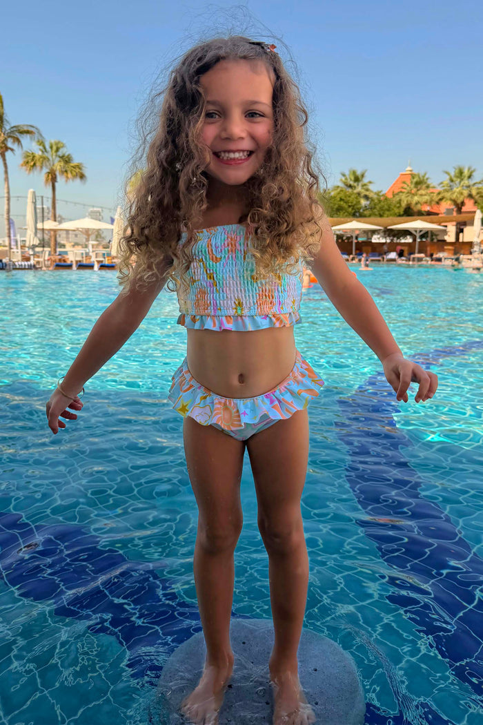 Blue Starburst Crop Bikini Set with a smocked top and frill trims, worn by a girl in a sunny vacation pool.