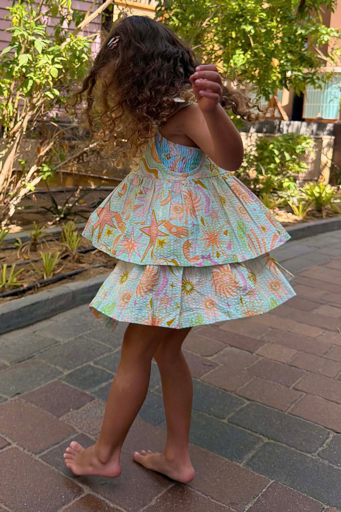 Girl's Starburst Skirt Co-ord Set in blue cotton with a pink sun and star print, worn outdoors.