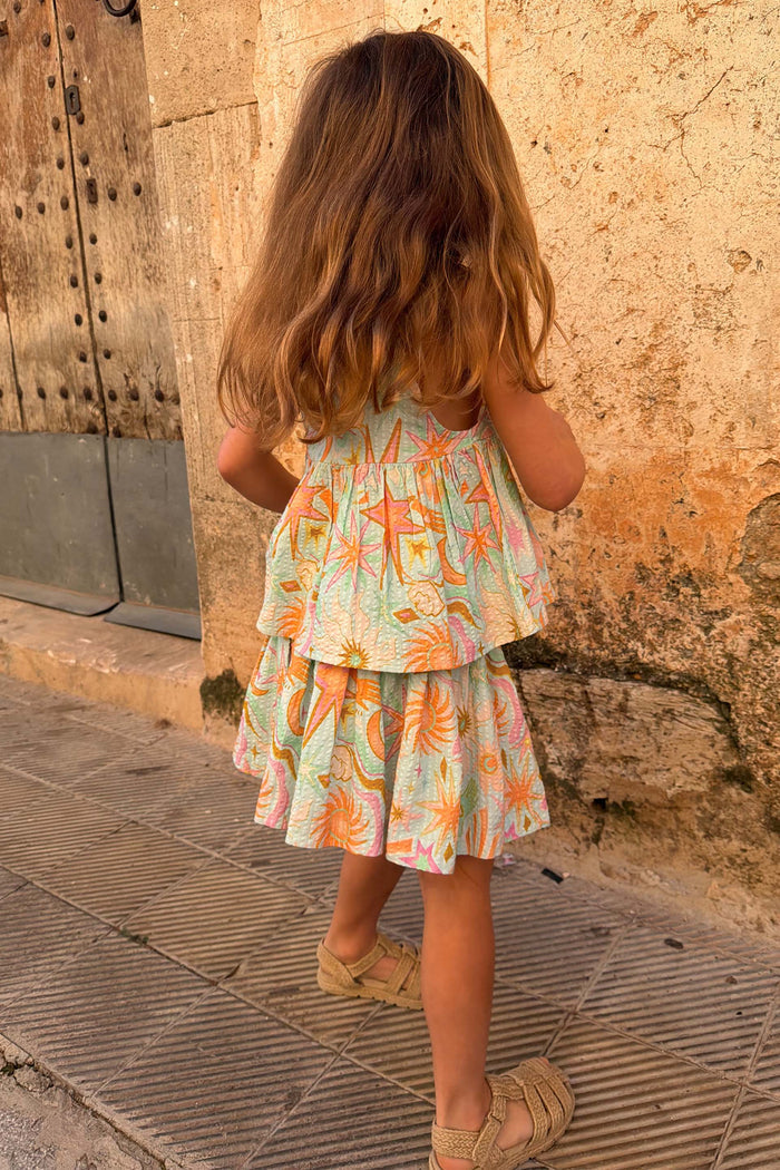 Girl's blue cotton Starburst Skirt Co-ord with a sun and star print, peplum top and tiered skirt, seen from behind.