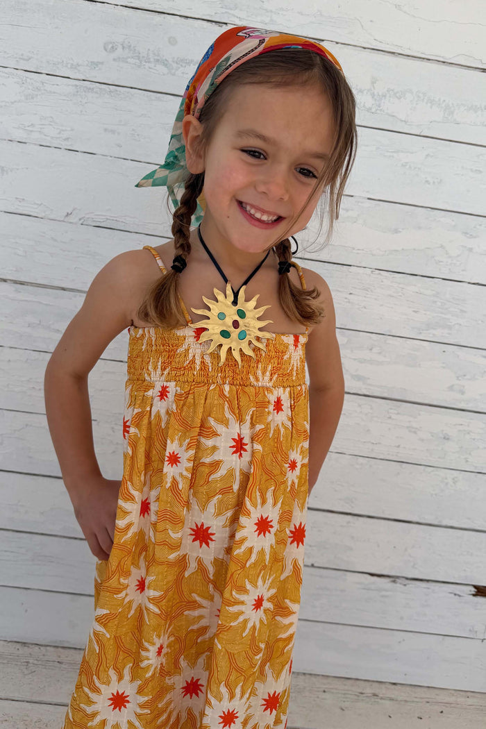 NFD Kids Yellow Cotton Sun Dress with an orange sun print and shirred bodice, worn by a young girl.