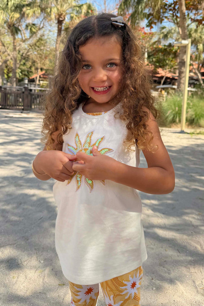 Girl’s Yellow Sun Cotton Set featuring a cream sequinned sun vest and yellow soleil motif trousers in a vacation setting.