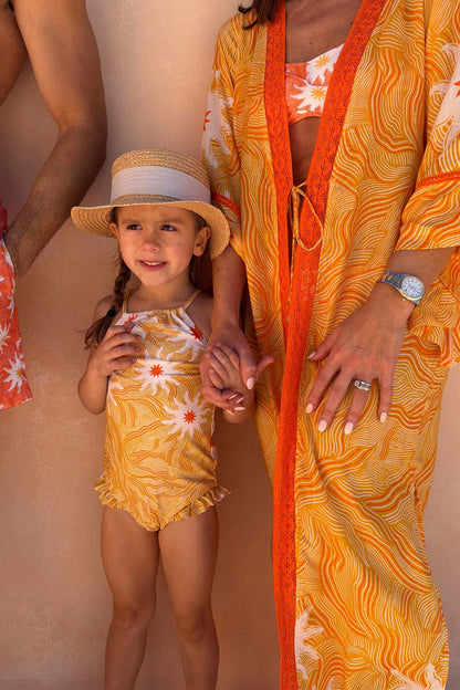 Yellow sun print swimsuit with frill details on a young girl wearing a straw hat on vacation.