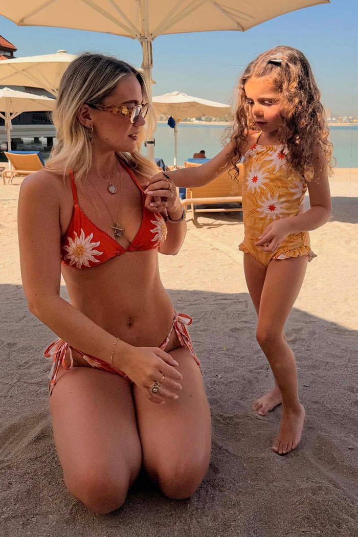 Girl's Yellow Sun Swimsuit with frill trim and sun print, paired with a matching adult bikini on a beach vacation.
