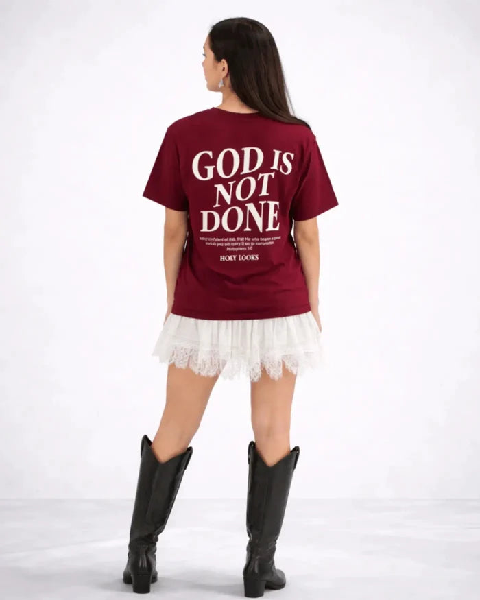 Person wearing a maroon t-shirt with 'GOD IS NOT DONE' text on the back, standing against a white background.