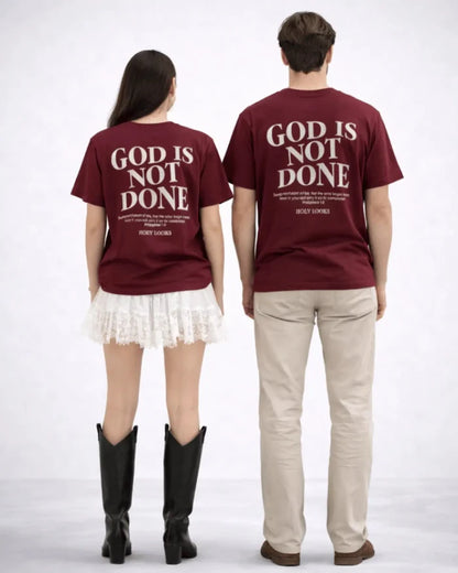 Two people wearing maroon t-shirts with 'GOD IS NOT DONE' text on a white background