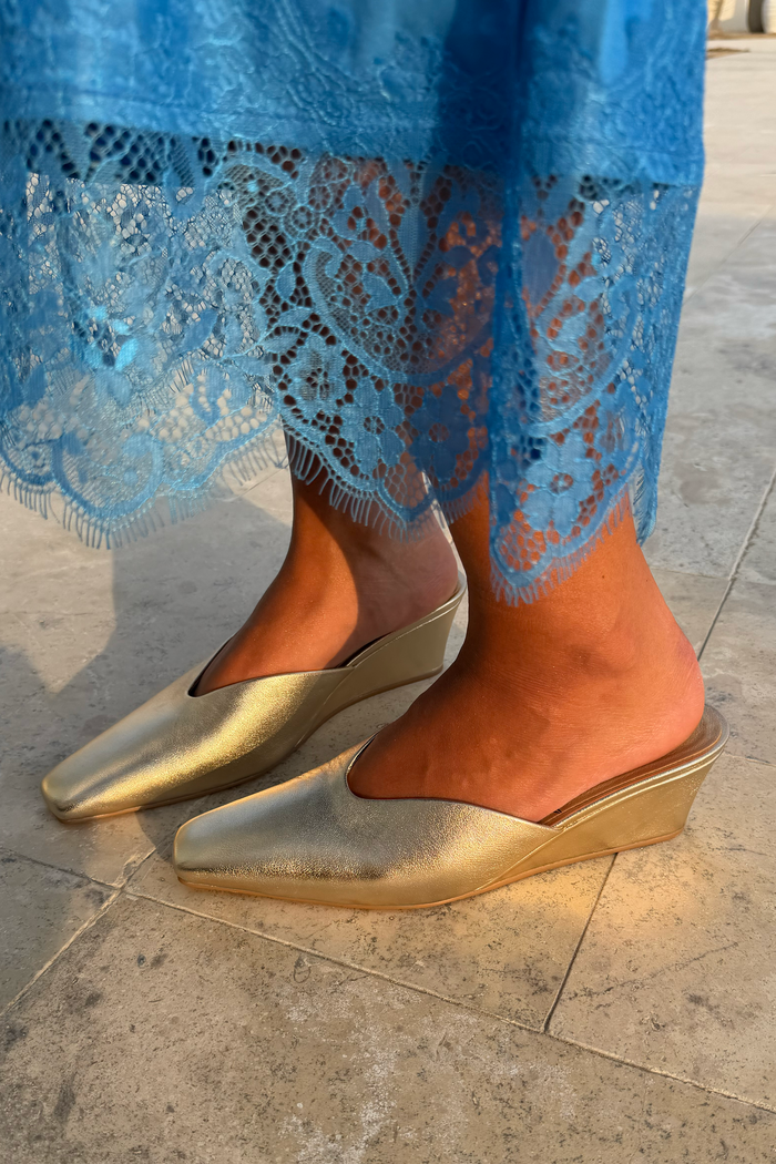 Metallic Gold Wedge Mule with a pointed toe and sculpted heel, paired with a blue lace dress.