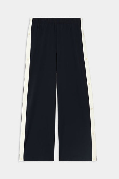 The SPLITS59 Jordan Nylon Twill Tearaway pants in Black/Creme are wide-leg pants crafted from a nylon-spandex blend, featuring white snap button panels running down the sides, and are displayed flat against a white background.