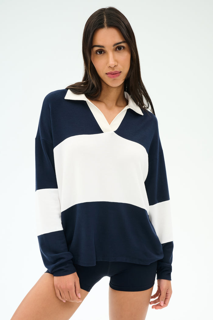 A woman wears the SPLITS59 Katie Fleece Rugby in Indigo/White with navy shorts, standing against a plain light background.