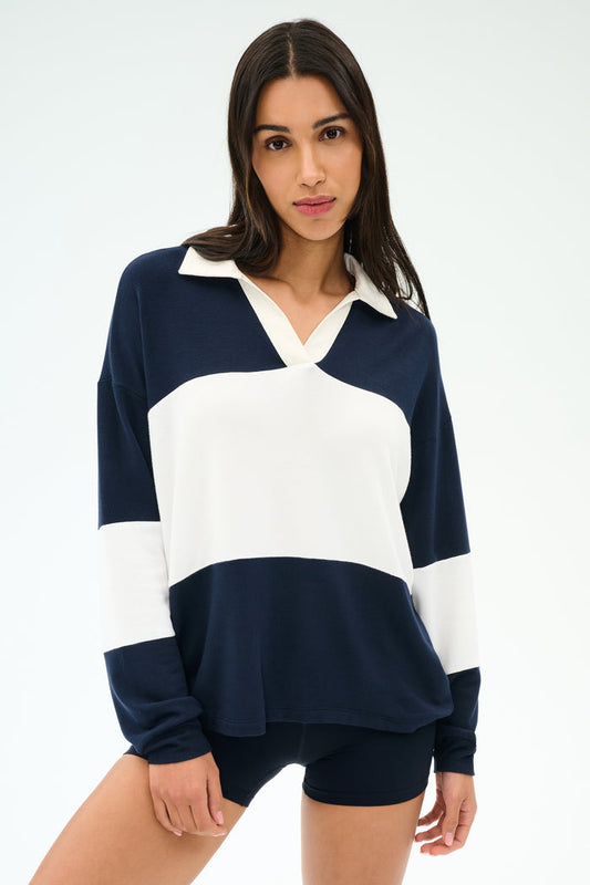 A woman wears the SPLITS59 Katie Fleece Rugby in Indigo/White with navy shorts, standing against a plain light background.