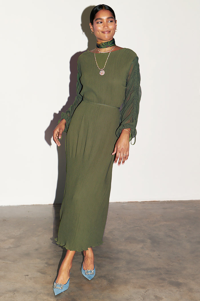 Khaki Celia Plisse Dress with long sheer sleeves and a pleated finish, styled with blue embellished heels.