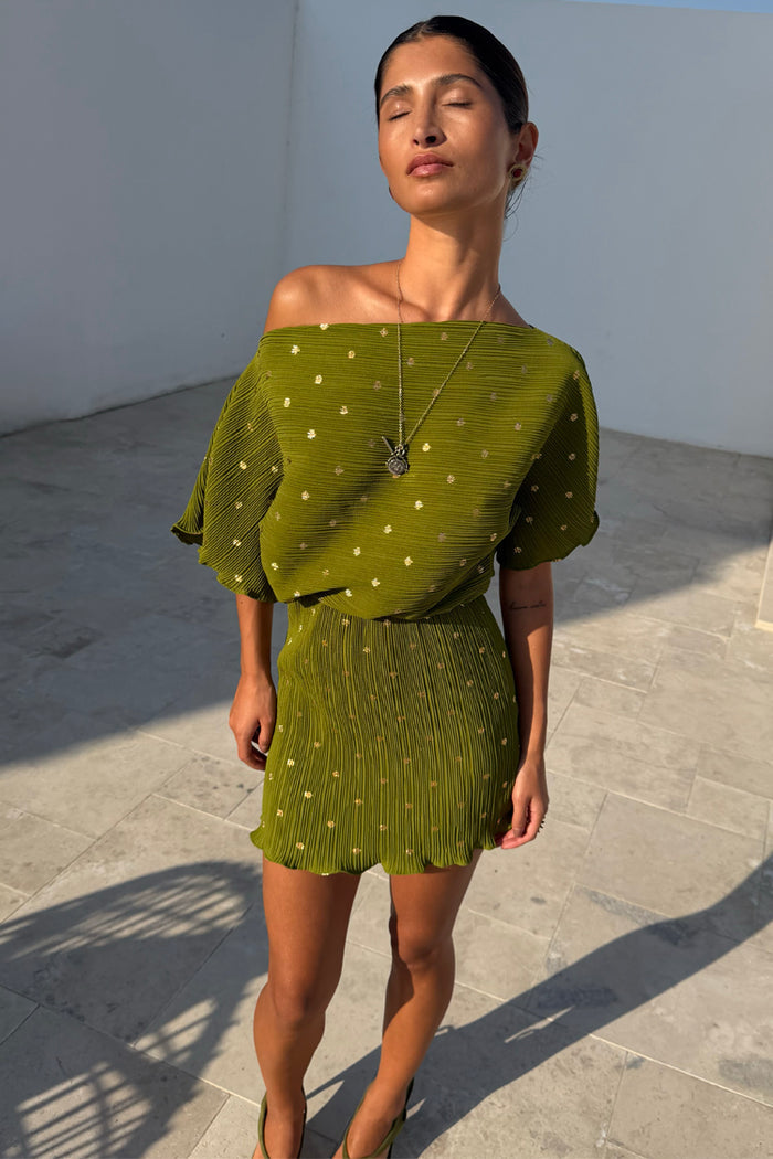 Khaki Tilly mini dress in plisse fabric with a gold fleck print and off-the-shoulder neckline, shown in the sun.