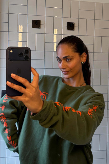 Khaki Sweatshirt with orange embroidered motifs on the sleeves and an oversized fit, shown in a casual selfie.