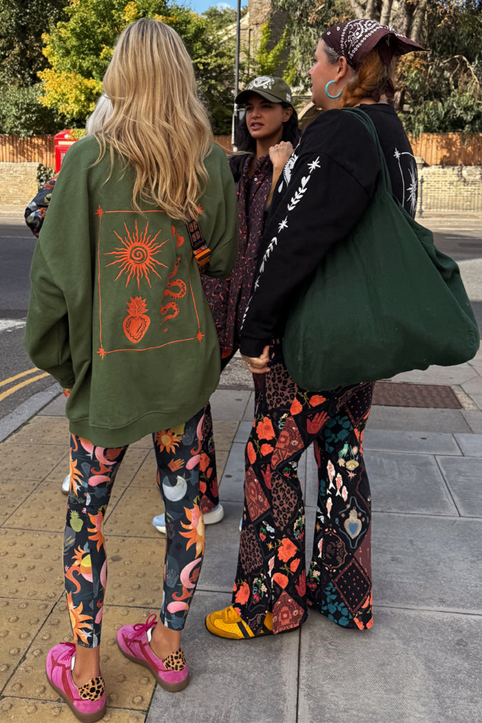 Khaki sweatshirt with orange sun embroidery, styled for a London look with patterned leggings.
