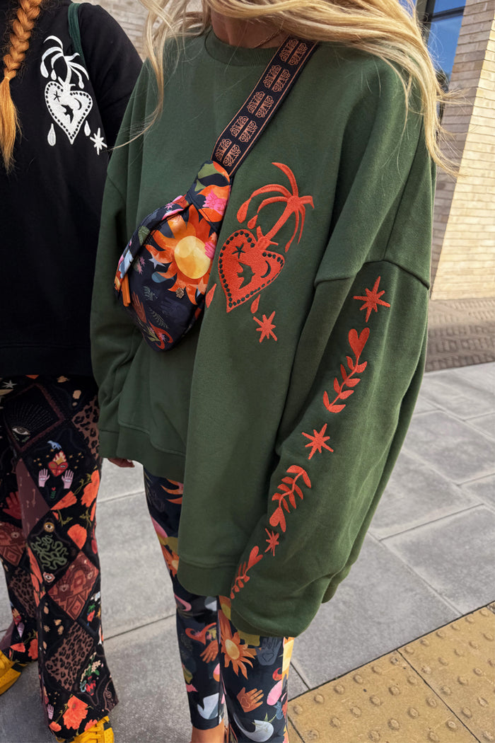 Khaki sweatshirt featuring orange heart and palm embroidery on the chest and star motifs along the sleeve.