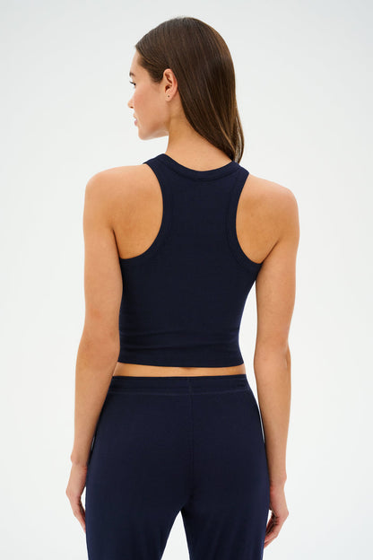 Facing away, a person with long brown hair wears the "Kiki Rib Crop Tank - Indigo" by SPLITS59 with matching pants made from baby rib fabric against a plain background, as if set for gym workouts.