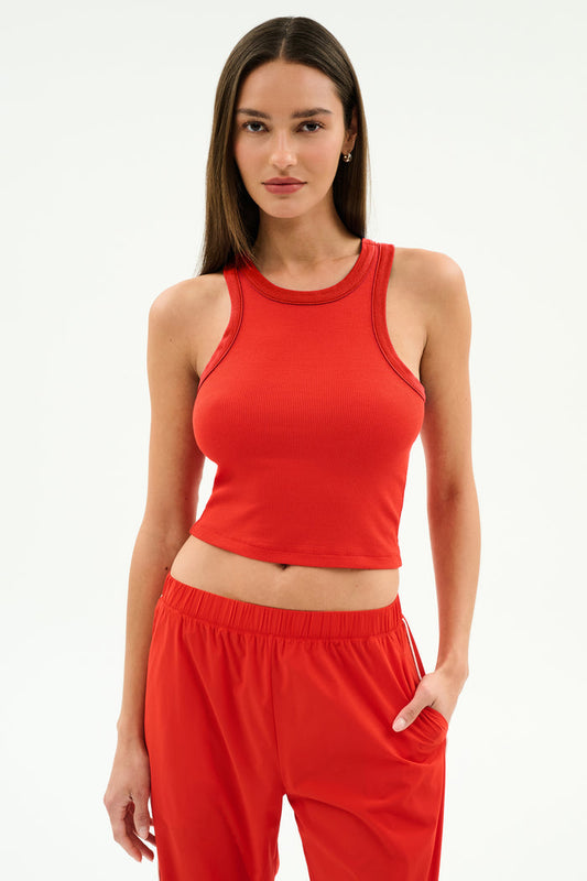 A person stands against a plain background wearing the SPLITS59 Kiki Rib Crop Tank in Lotus Red with matching red pants, one hand in a pocket—ideal for gym sessions or casual outings.