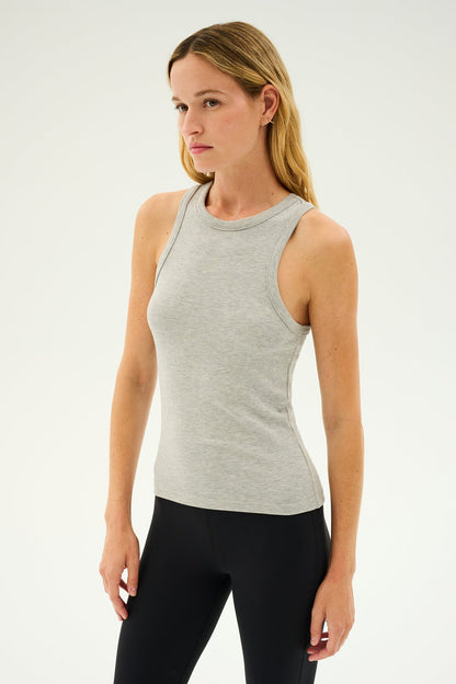 A person with long hair wearing the SPLITS59 Kiki Rib Tank Full Length in Heather Grey and black pants, standing against a plain background, ready for yoga.
