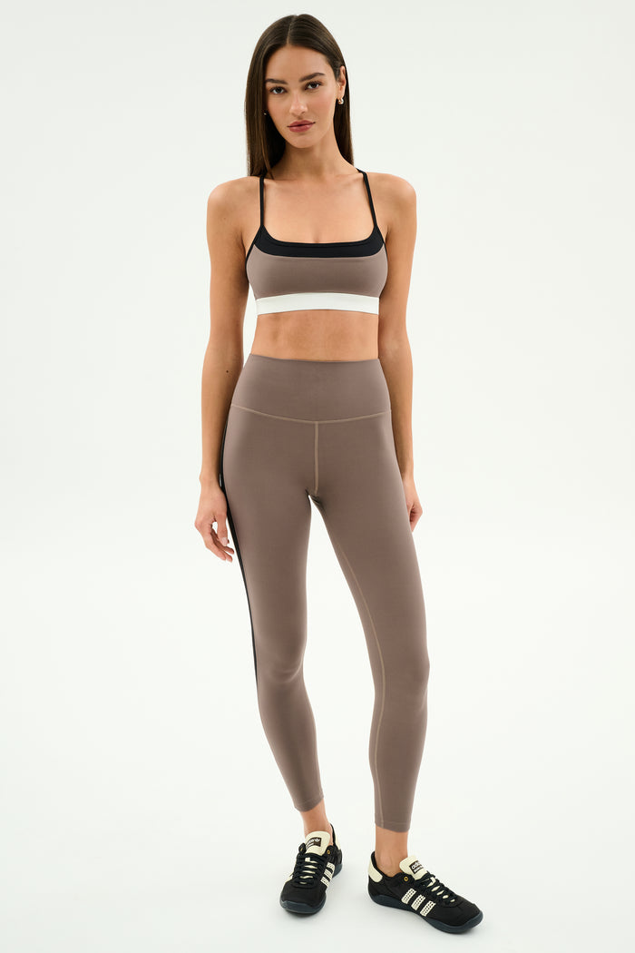 A woman poses against a plain background in SPLITS59's Layla Airweight High Waist 7/8 leggings in Lentil/Black—breathable and perfect for hot yoga.