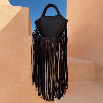 Black Leather Bag with long fringe detail and a plaited handle against beige architectural stone steps.