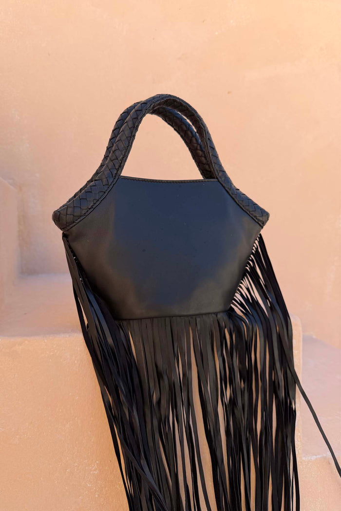 Black Leather Fringe Bag with a plaited handle and long fringe details, resting on a neutral stone background.