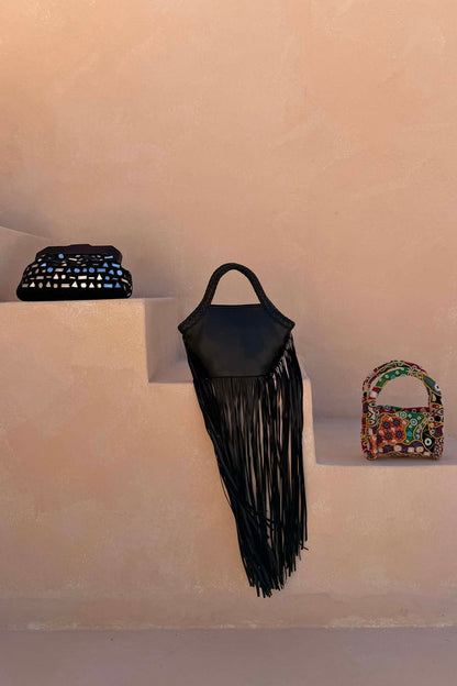 Black Leather Fringe Bag with long tassels and a plaited handle, styled on neutral steps with other bags.