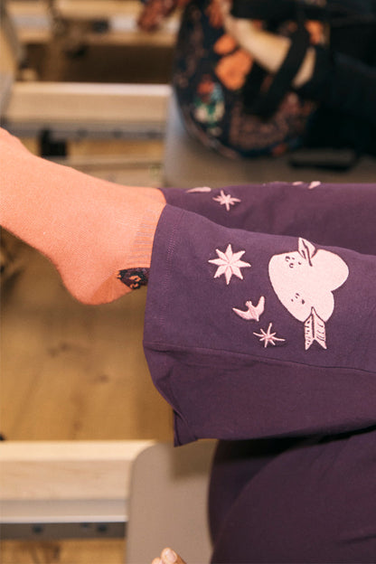 Orange cotton crew sock with leopard print detail worn with embroidered purple trousers in a gym.