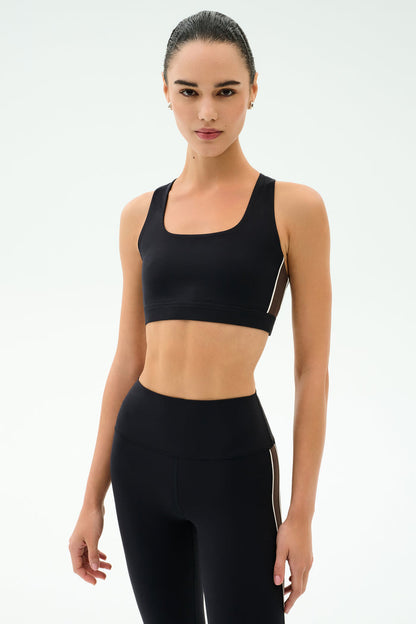 A woman stands facing forward in the SPLITS59 Lexi Rigor Bra - Black/Dark Chocolate, ideal for gym workouts, against a plain white background.