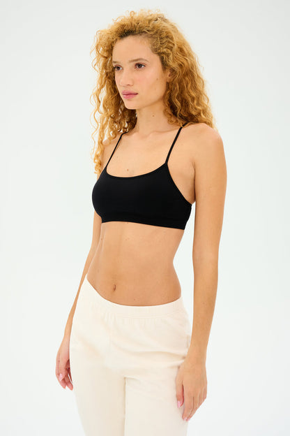 A person with long curly hair, confidently wearing the Splits59 Loren Seamless Bra in black and white pants, stands against a plain background.