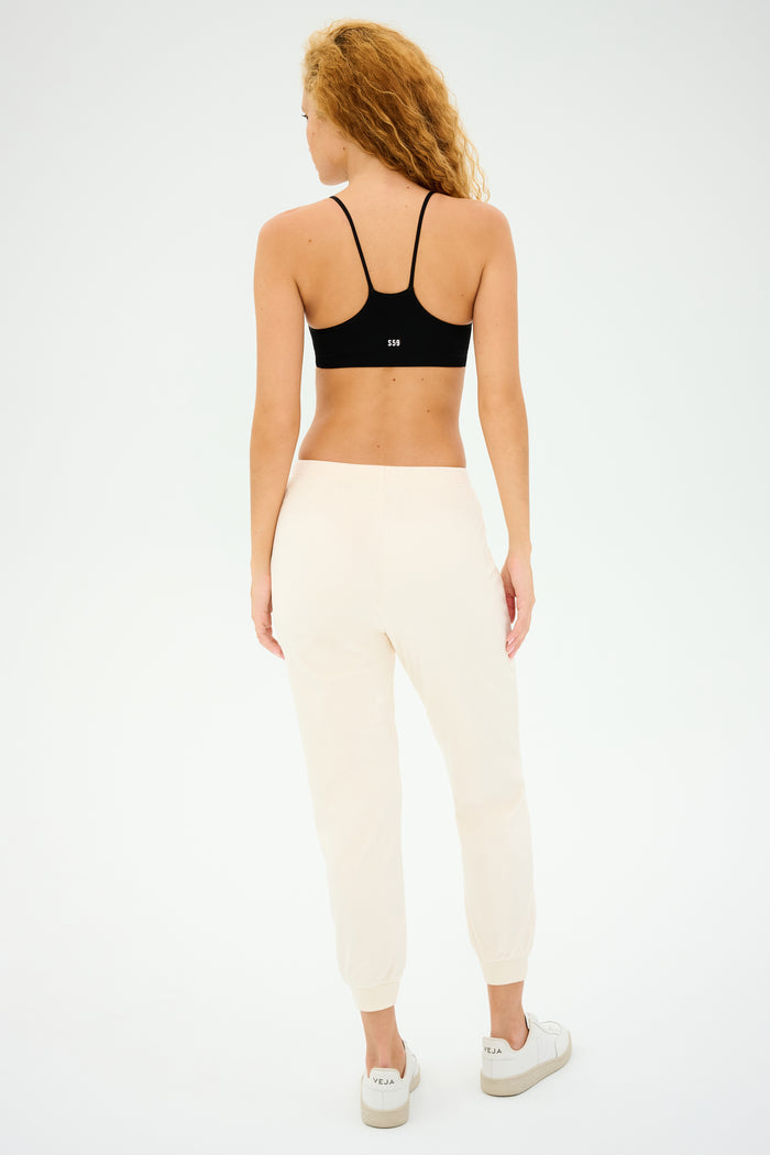 A curly-haired person stands with their back to the camera, poised for gym workouts in a Splits59 Loren Seamless Bra - Black, light joggers, and white sneakers against a plain backdrop.