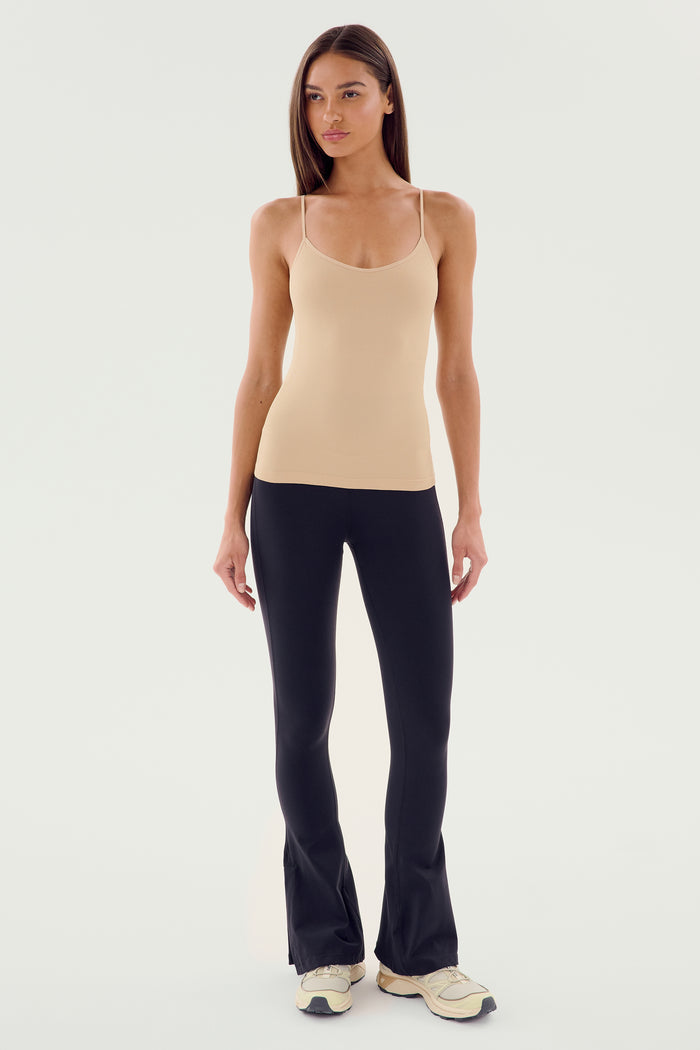 A person stands against a plain background wearing the Loren Seamless Waist Length Tank in Nude by SPLITS59, paired with black pants and white sneakers—perfect for gym workouts.