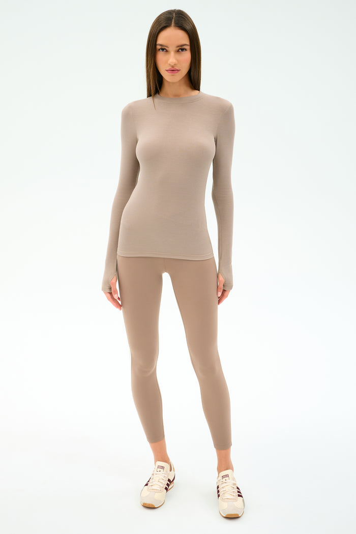 A woman faces forward in the SPLITS59 Louise Rib Long Sleeve - Latte and matching leggings—ideal beige-toned activewear for gym workouts—with white sneakers, set against a plain light background.