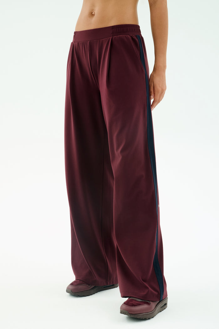 A person wears SPLITS59's Luca Airweight Trouser with Stripe in Dark Cherry/Indigo, paired with black shoes, standing against a plain light background.