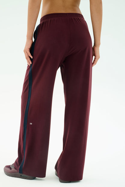 A person stands with their back to the camera, wearing SPLITS59's Luca Airweight Trouser with Stripe in Dark Cherry/Indigo, crafted from a comfy nylon-spandex blend, paired with matching shoes.
