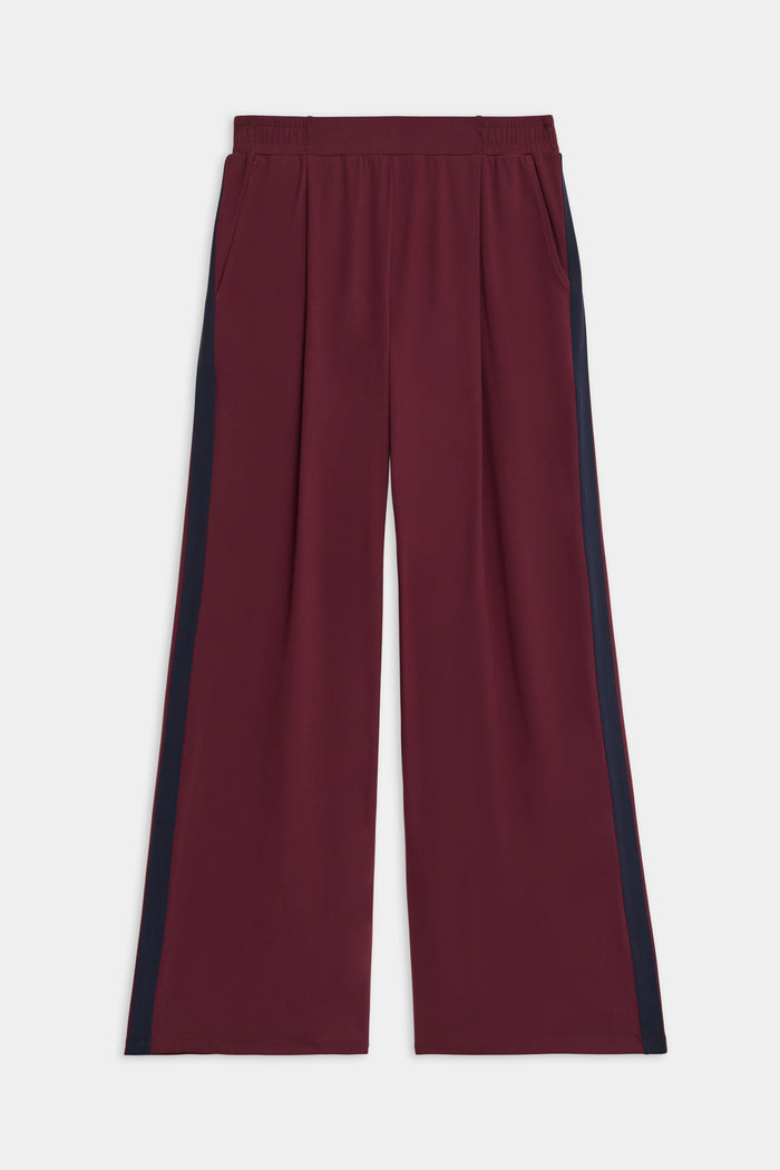 The SPLITS59 Luca Airweight Trouser with Stripe features a wide-leg maroon design, navy side stripes, an elastic waistband, and side pockets, shown laid flat on a white background.
