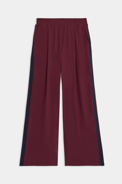 The SPLITS59 Luca Airweight Trouser with Stripe features a wide-leg maroon design, navy side stripes, an elastic waistband, and side pockets, shown laid flat on a white background.
